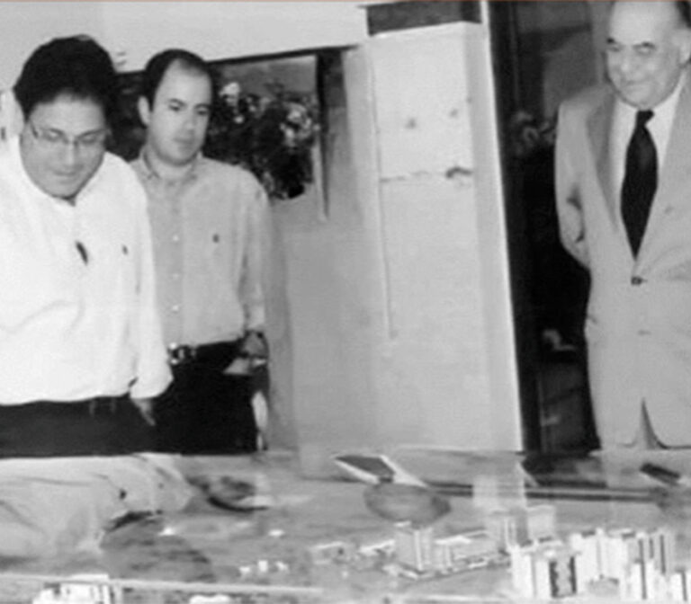 Três homens observam a maquete de um empreendimento, em foto em preto e branco
