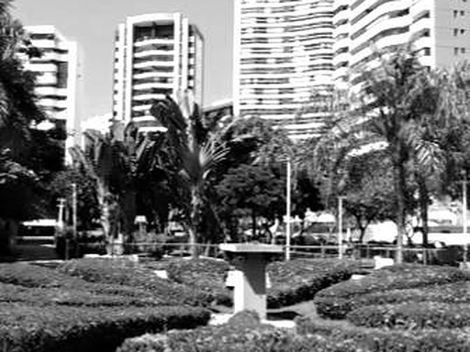 Praça com jardim e torres ao fundo, em preto e branco